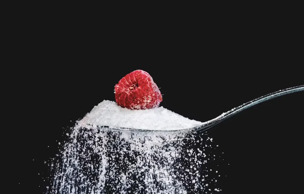 Cuillère de sucre blanc surmontée d’une framboise, fond noir